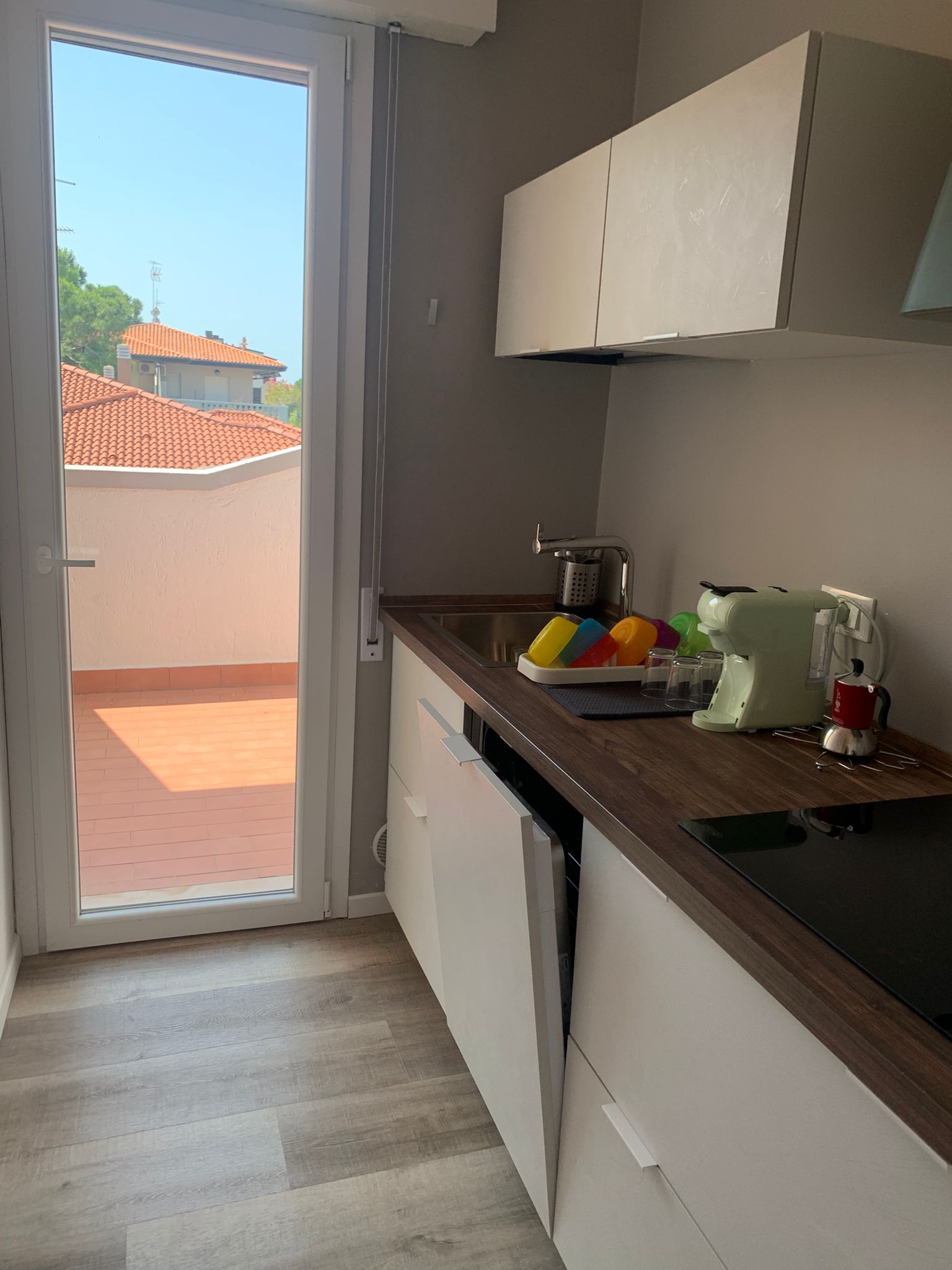 Cucina con mobili bianchi, piano in legno scuro, induzione, macchina da caffè verde e porta-finestra sul terrazzo
