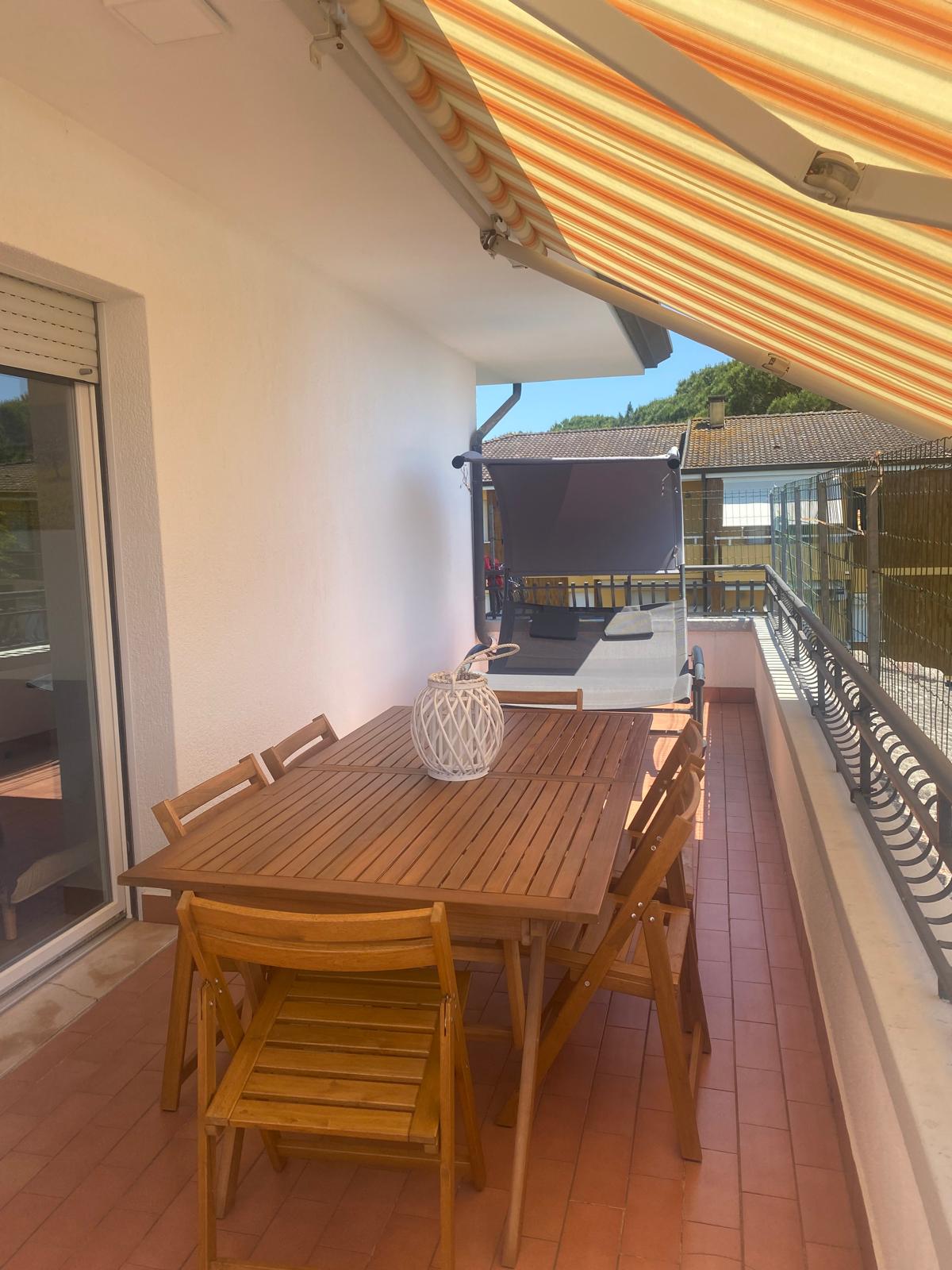 Terrazza con tenda a righe arancioni, tavolo e sedie pieghevoli in legno, lanterna bianca e pavimento in cotto